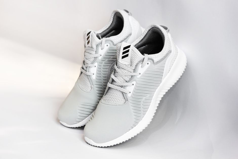 Pair of sports shoes with gray dense texture of surface and rubber inserts from sided and laces and white soles placed with heels up leaning on glance gray background
