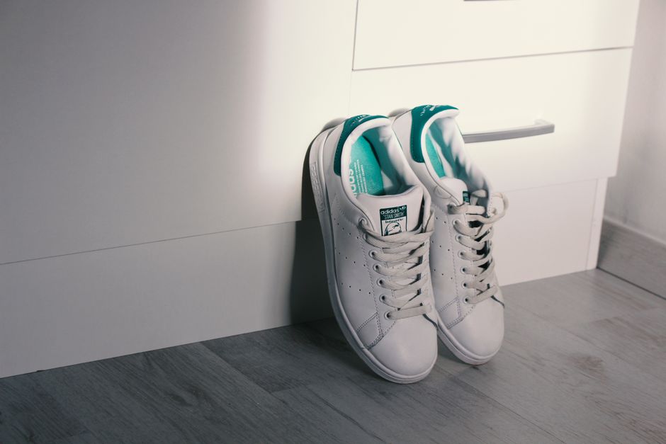 White Adidas sneakers with teal accents leaning against a drawer on a wooden floor.